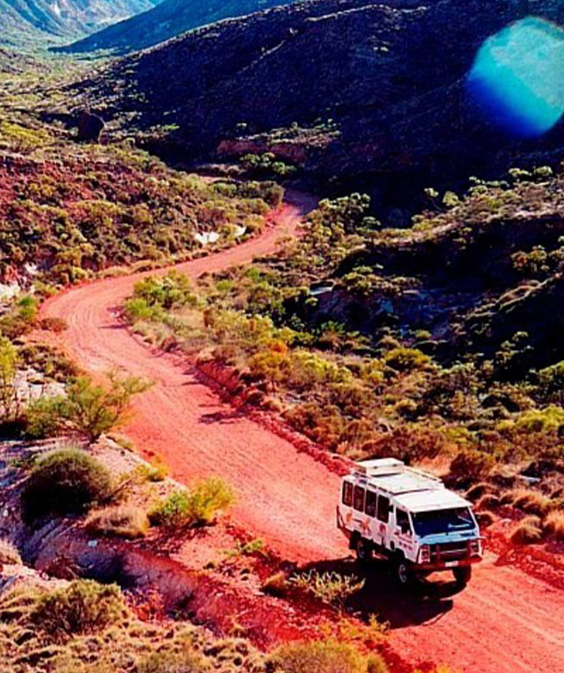 A Ningaloo Safari Tours bus on a red dirt road winding through the ranges