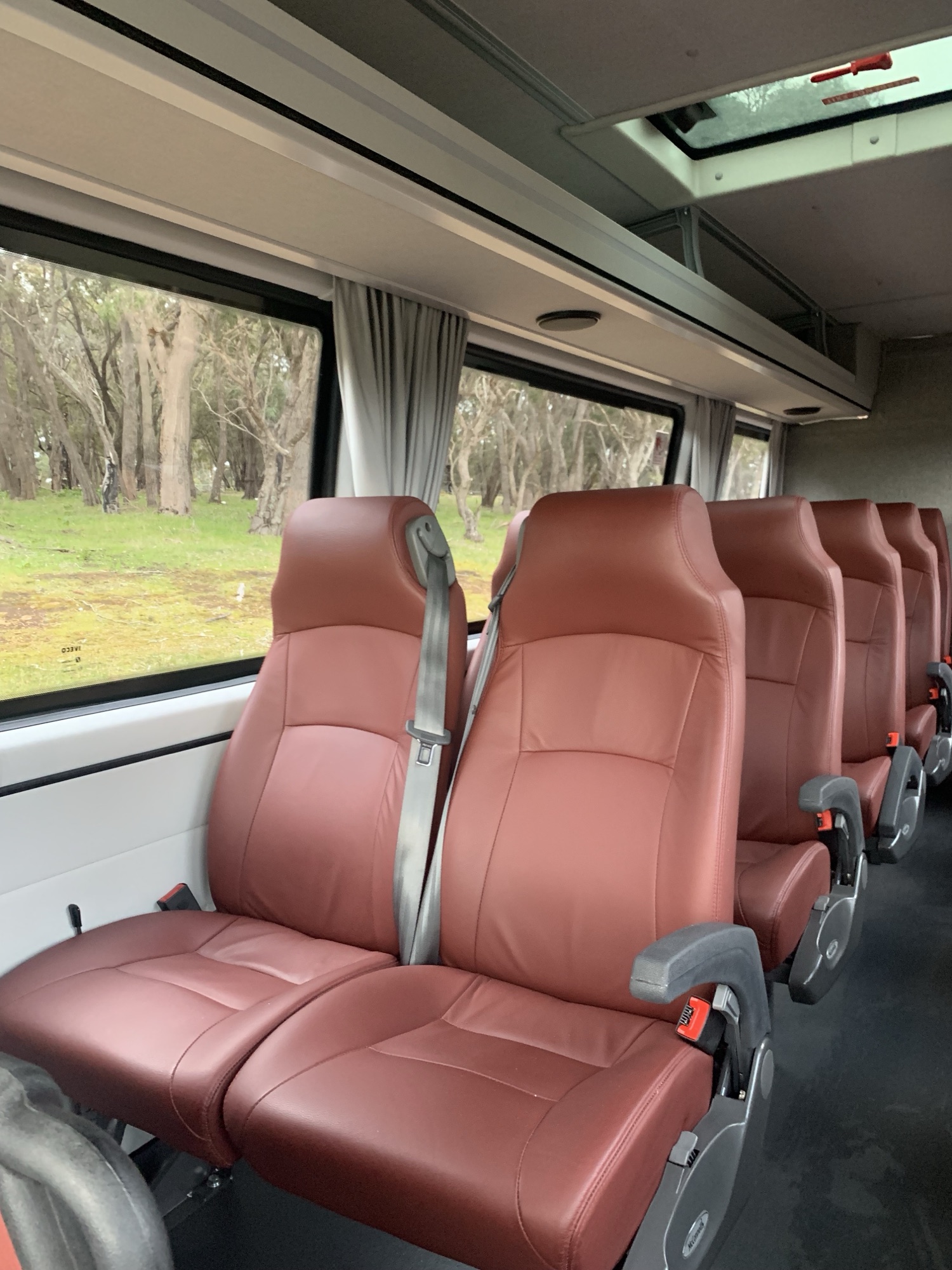 A pair of burgundy leather seats in the Iveco Daily beside a window, with a roof hatch above