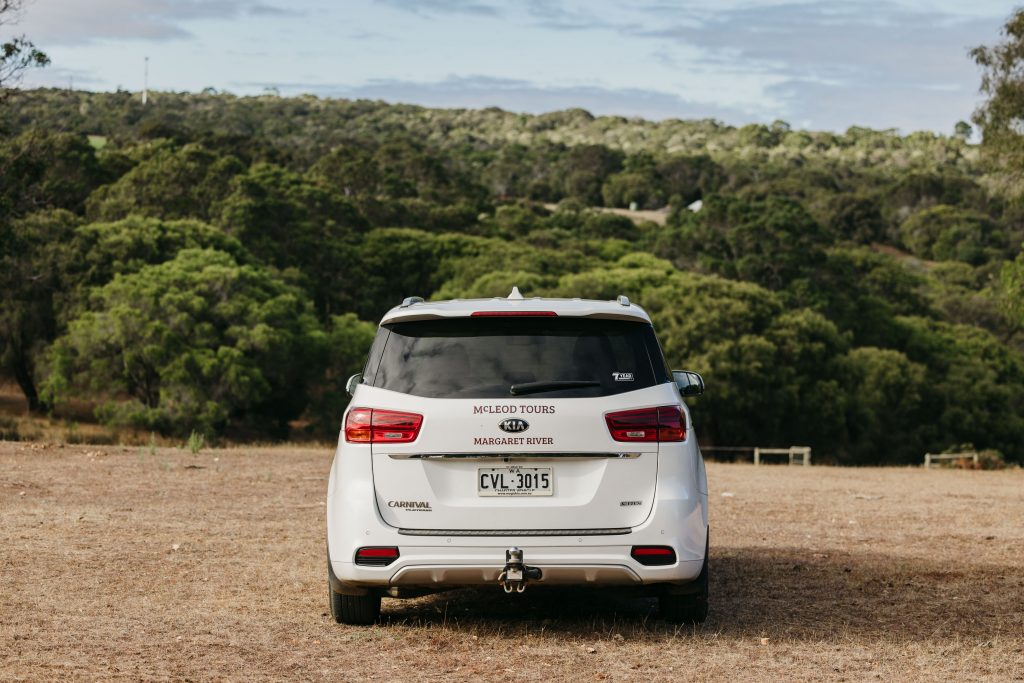 A white McLeod Tours Kia Carnival parked in a paddock at the farm