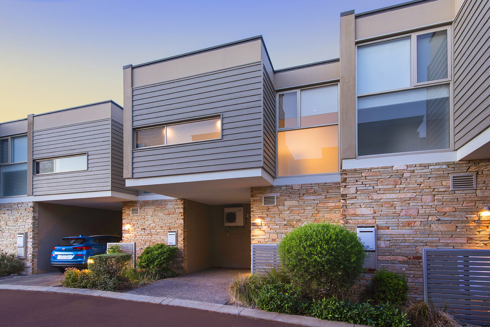 A two-storey resort building at dusk, stone and timber, carport below