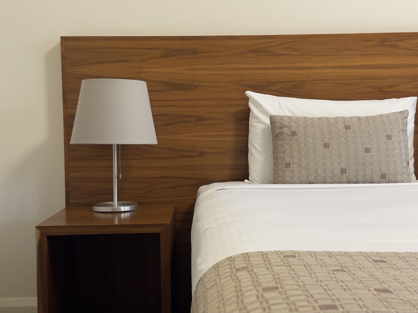 The bed against its timber headboard, bedside table and reading lamp alongside