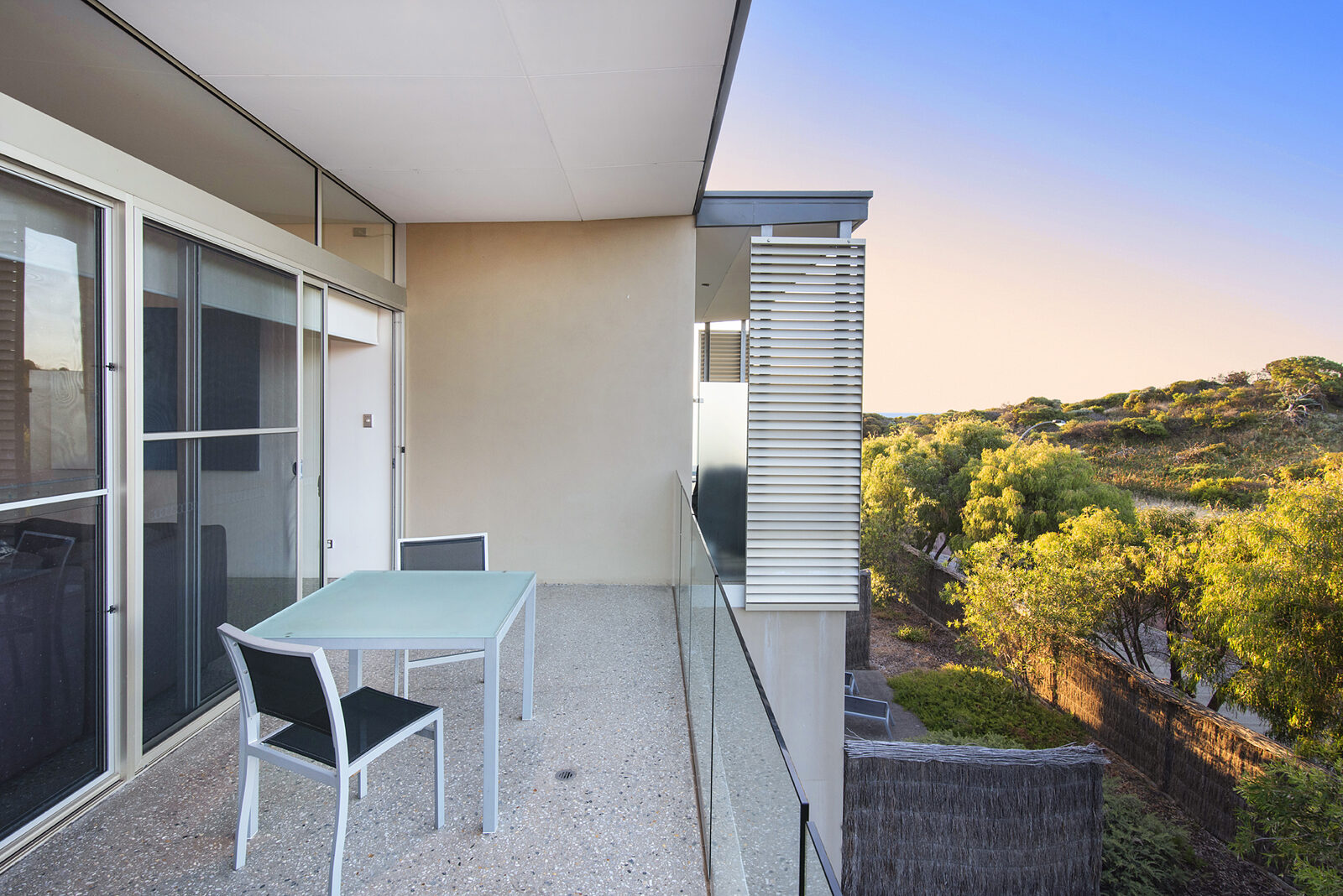 The private balcony at dusk, a table and two chairs above the treetops