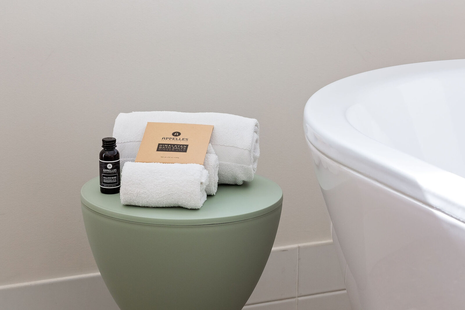 Rolled towels and bath oil on a stool beside the freestanding bath