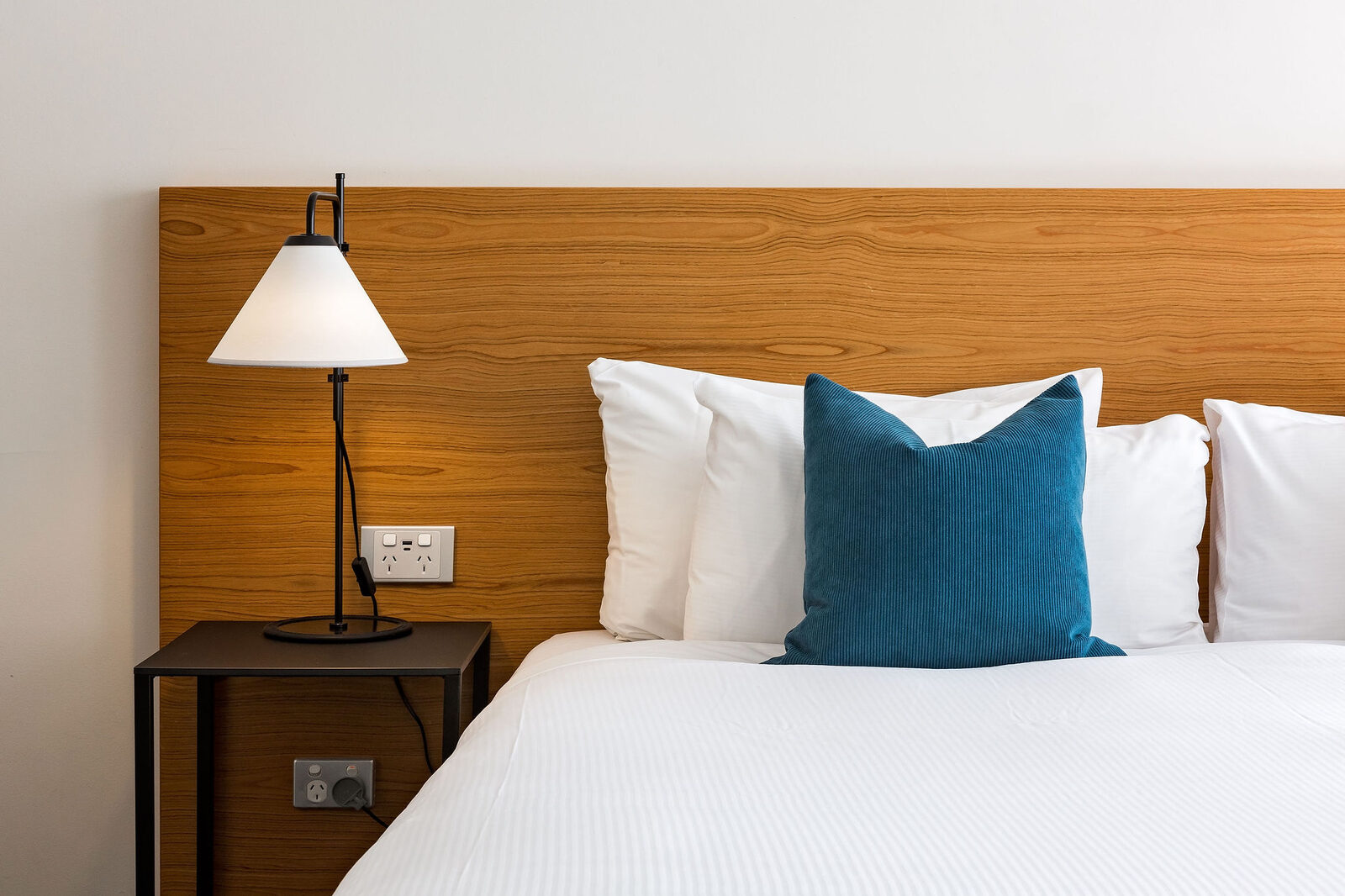 The king bed against its timber headboard, reading lamp to one side