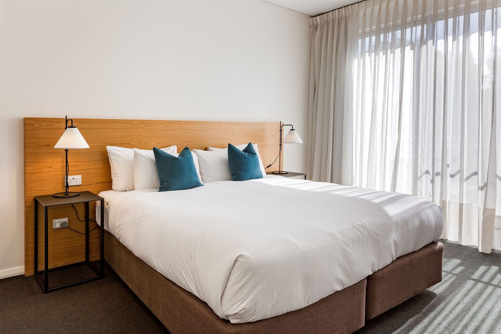 The bedroom, with a king bed and a full-height sheer-curtained window