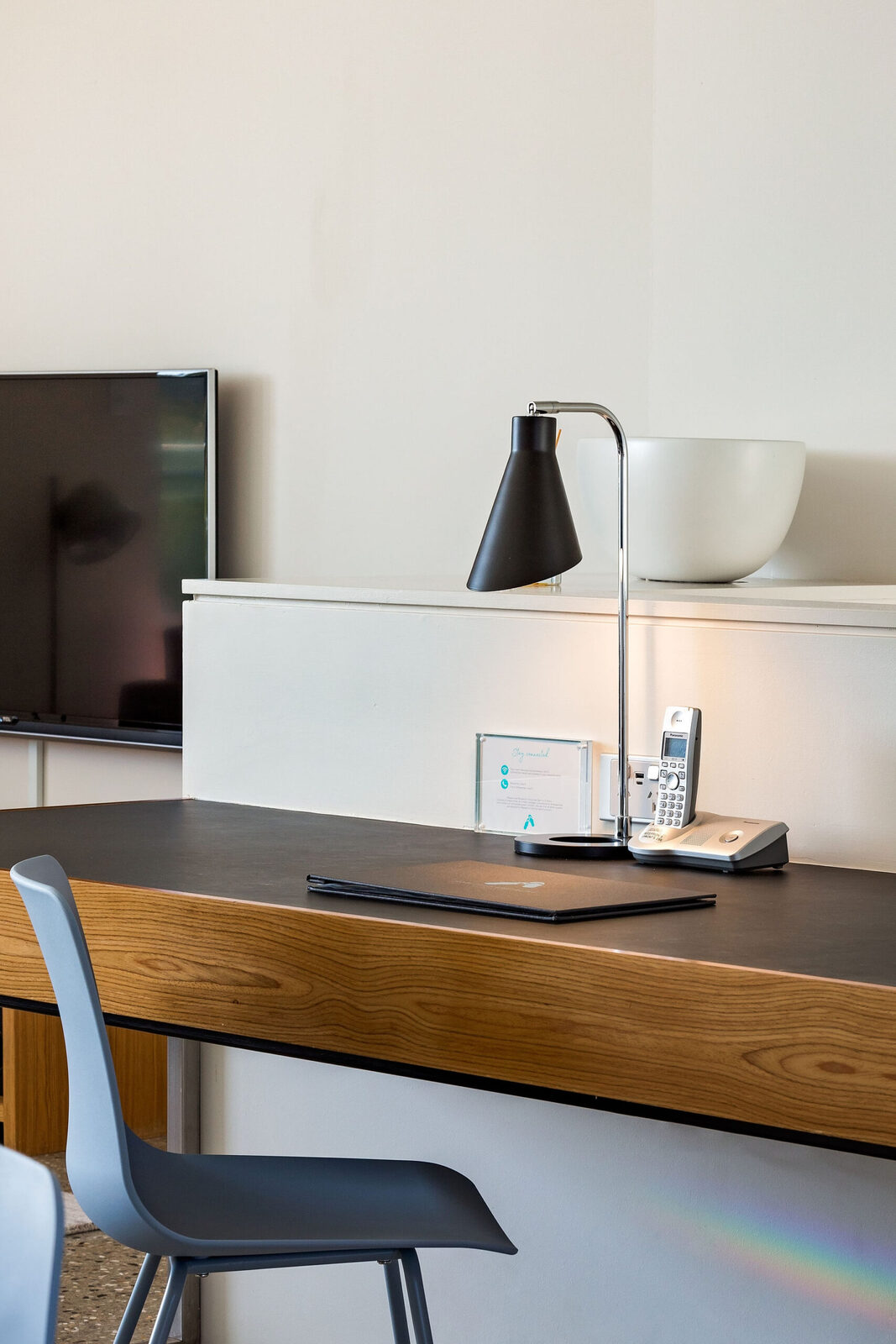 The timber desk with a task lamp and telephone, television on the wall behind