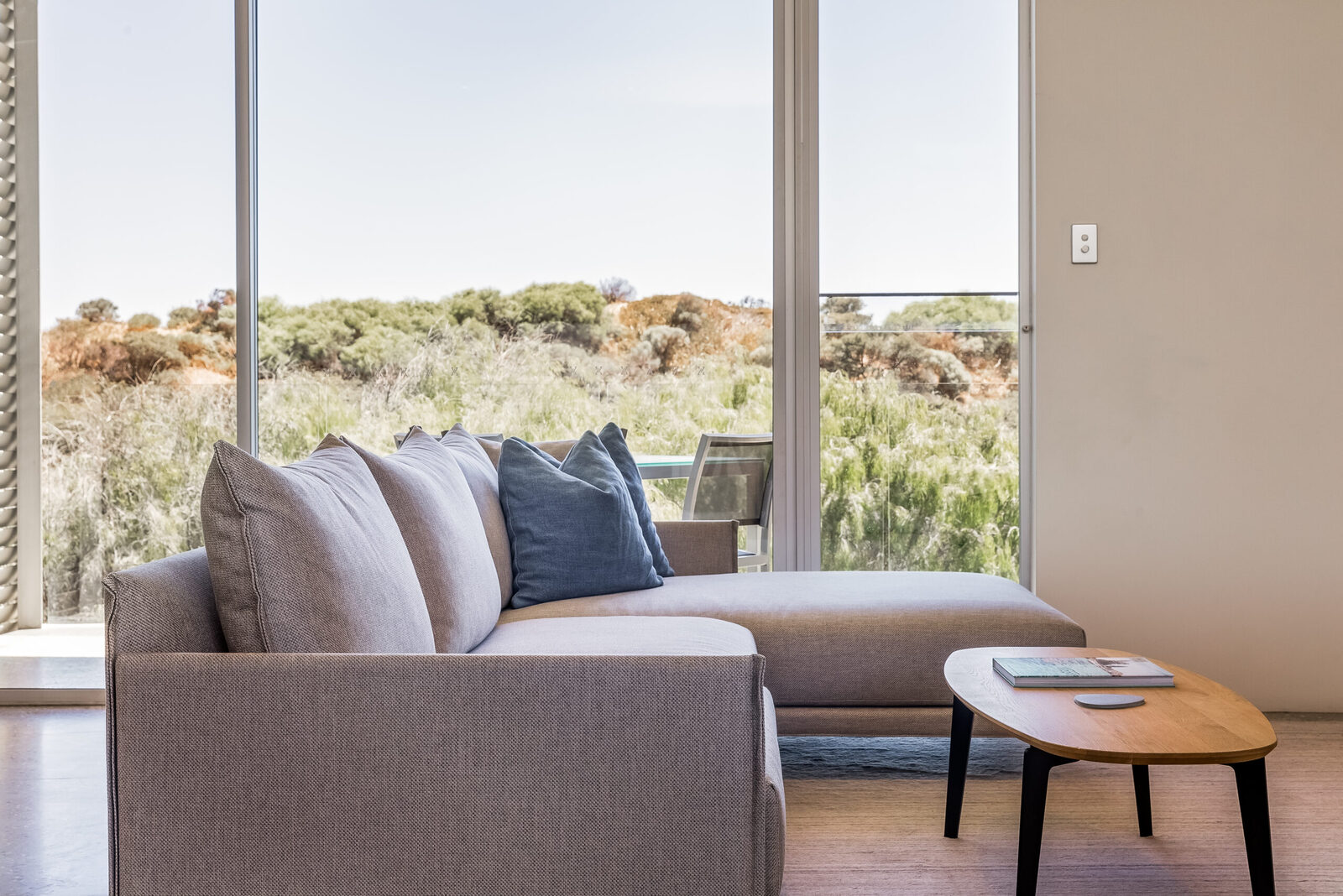 The sofa under floor-to-ceiling glass, looking out into the dune scrub