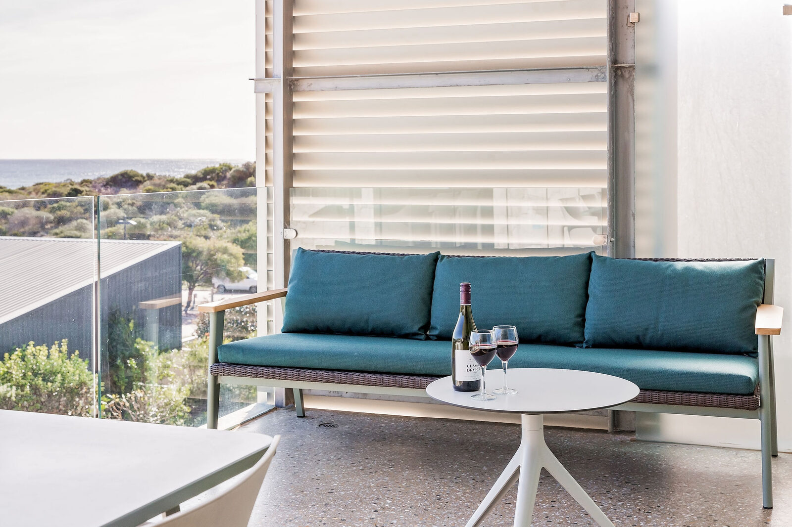 A teal outdoor sofa on the balcony, wine poured on the table beside it