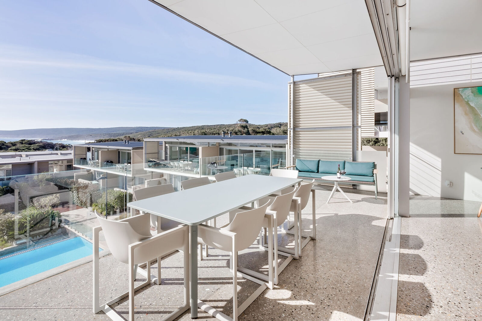 The balcony dining table under cover, the resort pool and the ocean below