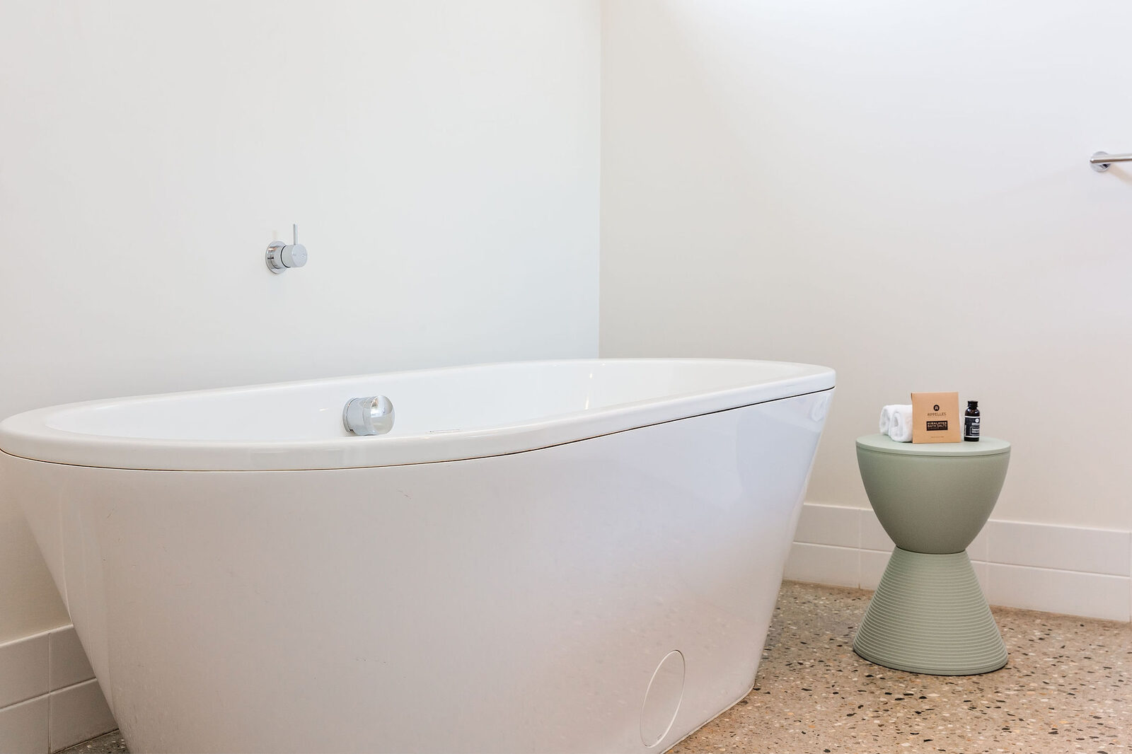 The freestanding bath, bath oil on a stool beside it