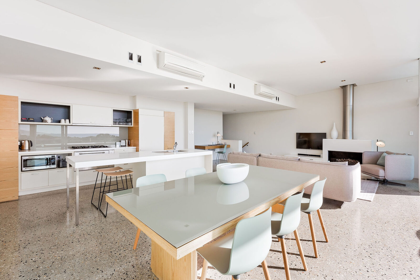 Dining table and kitchen island in one open room, ocean along the far wall