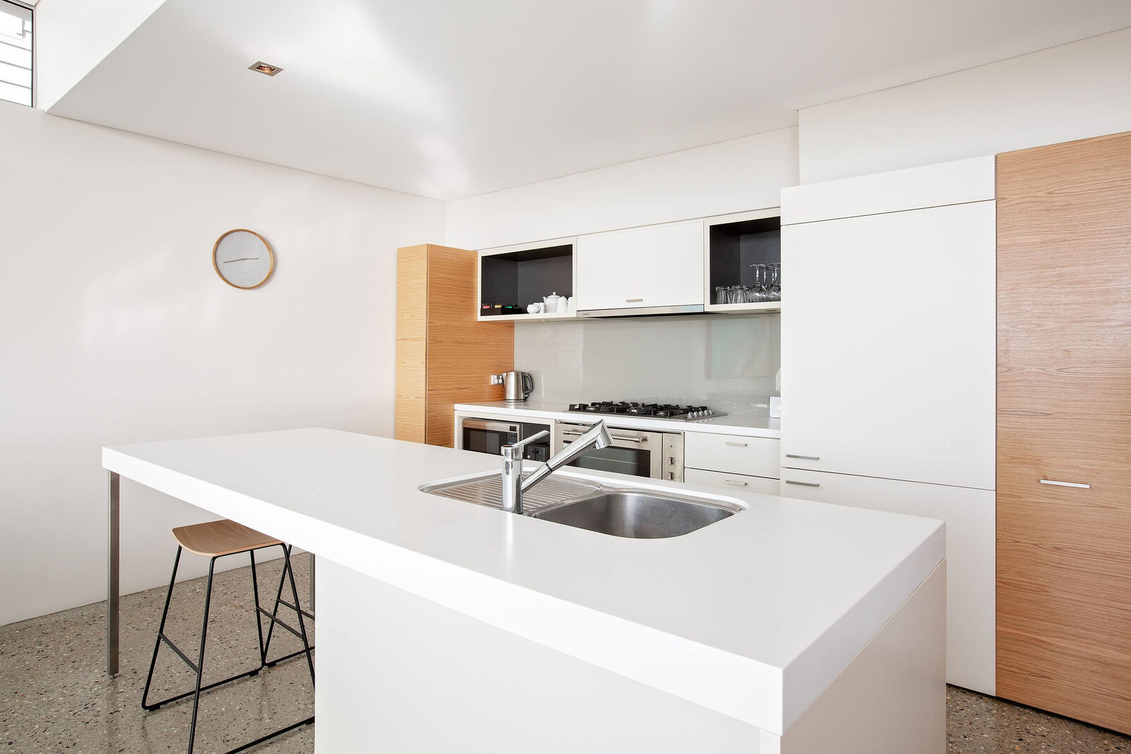 The full kitchen: stone island with sink, gas cooktop and oven in timber joinery