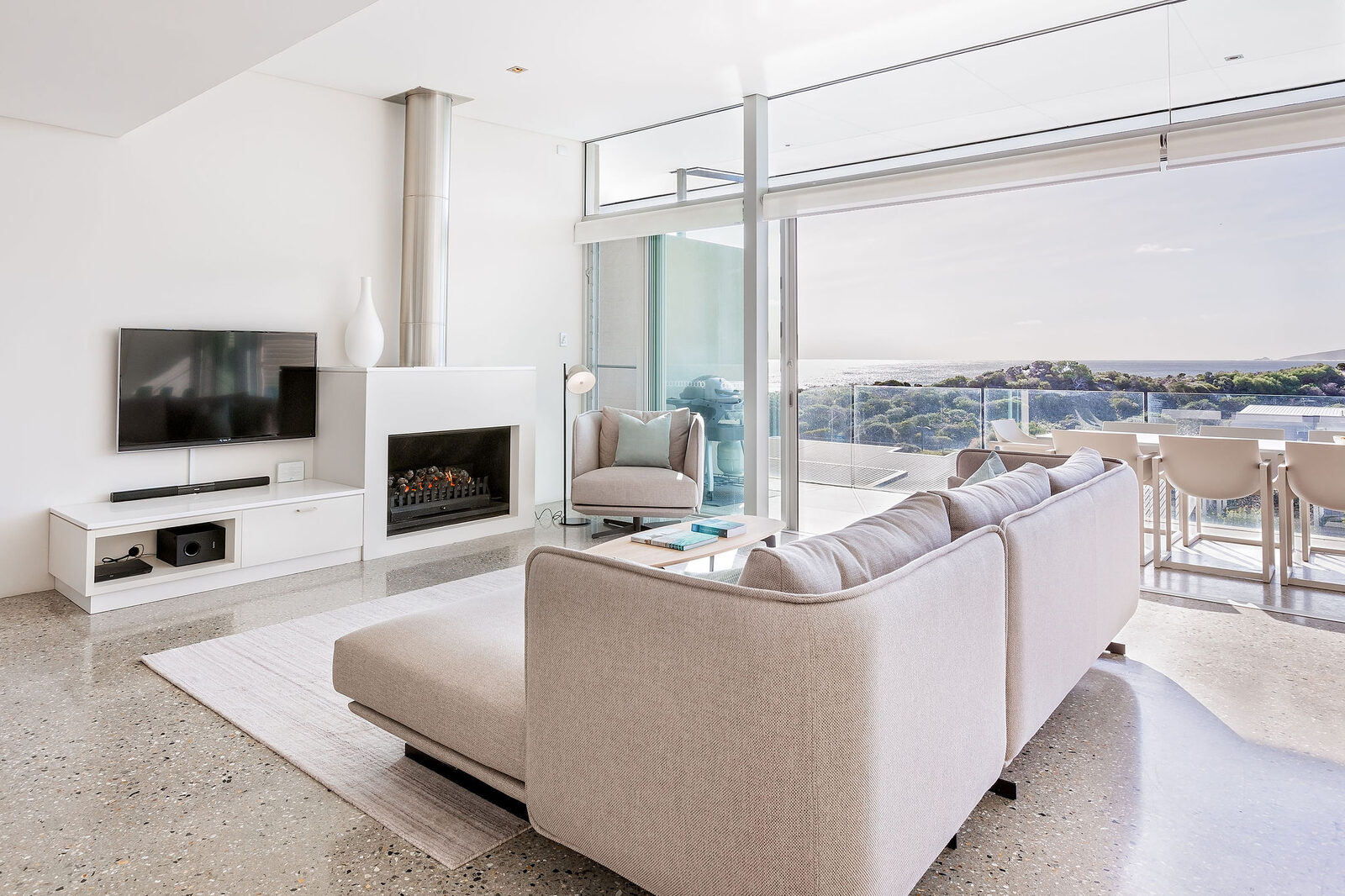The corner sofa facing the television and fireplace, ocean through the glass to the right