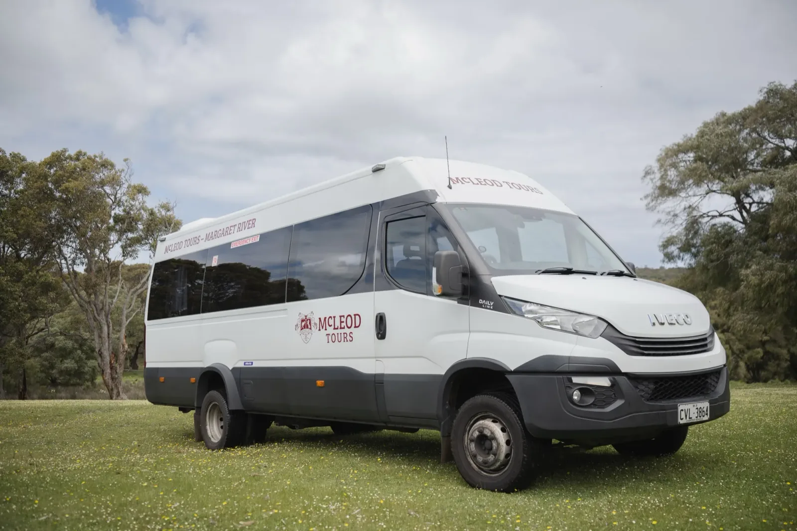 The white McLeod Tours Iveco Daily parked on grass with trees in the background 